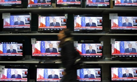 A woman walks past television screens showing Silvio Berlusconi&#039;s farewell speech Sunday: The controversial leader may be gone, but it won&#039;t be for long, say critics.