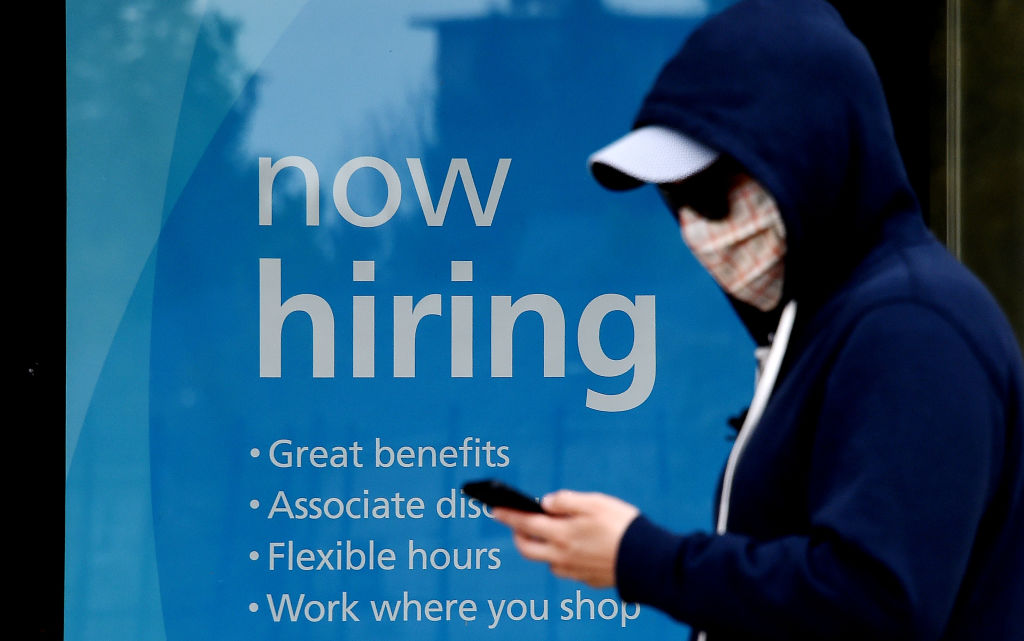 A man wearing a face mask walks past a sign &quot;Now Hiring&quot; in front of a store amid the coronavirus pandemic on May 14, 2020 in Arlington, Virginia