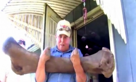 An Iowa man hefts the woolly mammoth femur bone he and his two sons found in the woods behind their house.