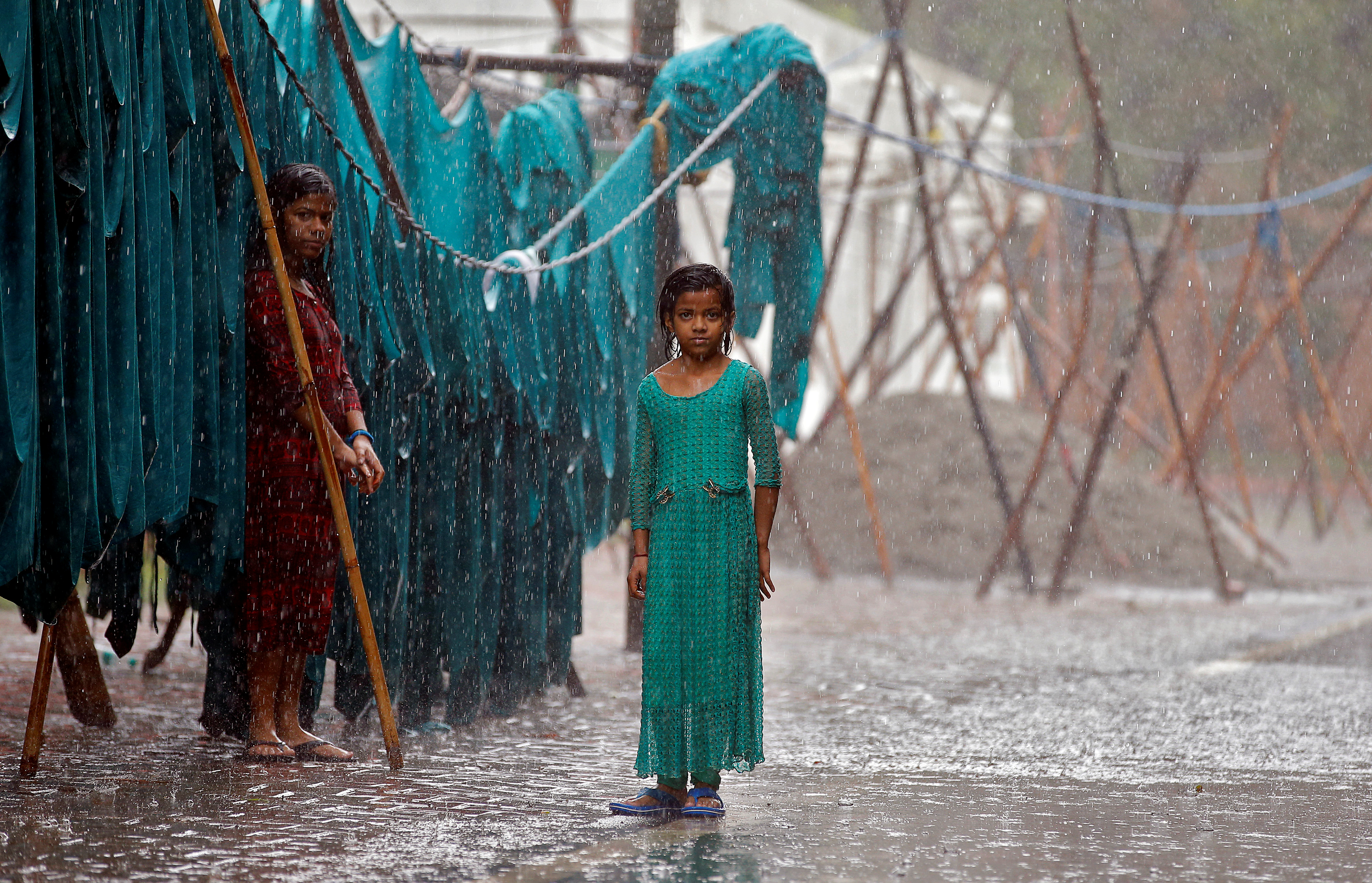 Girls stand in monsoon rains beside an open laundry in New Delhi, India.