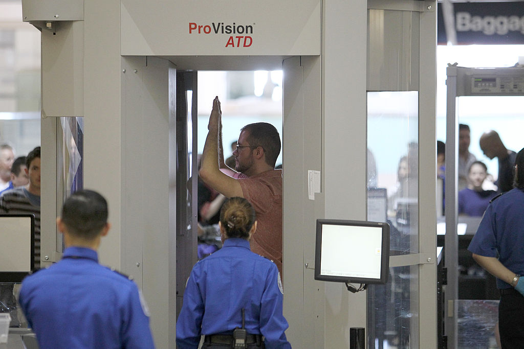 A passenger passes through a full-body scanner at a TSA checkpoint.