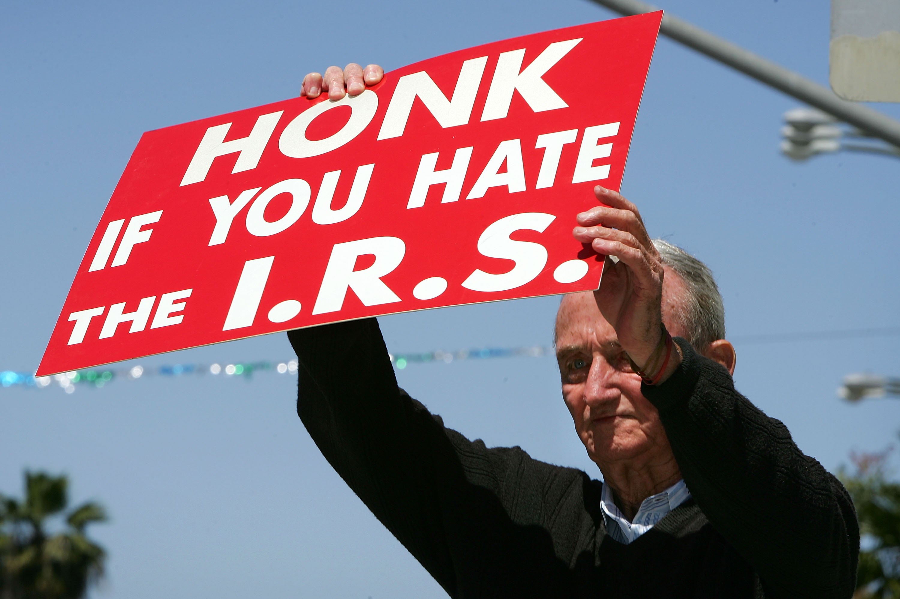 A man holds a sign that reads &quot;Honk if you hate the I.R.S.&quot;