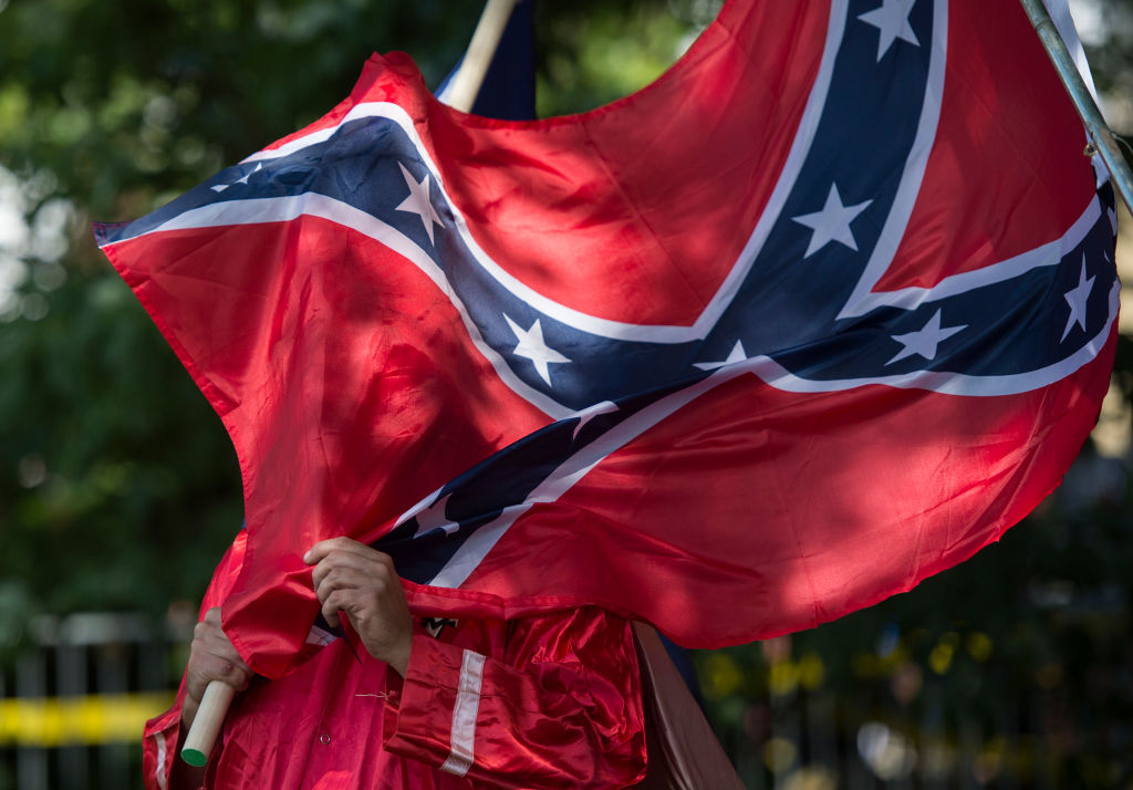 A protestor holds a confederate flag in front of his face.
