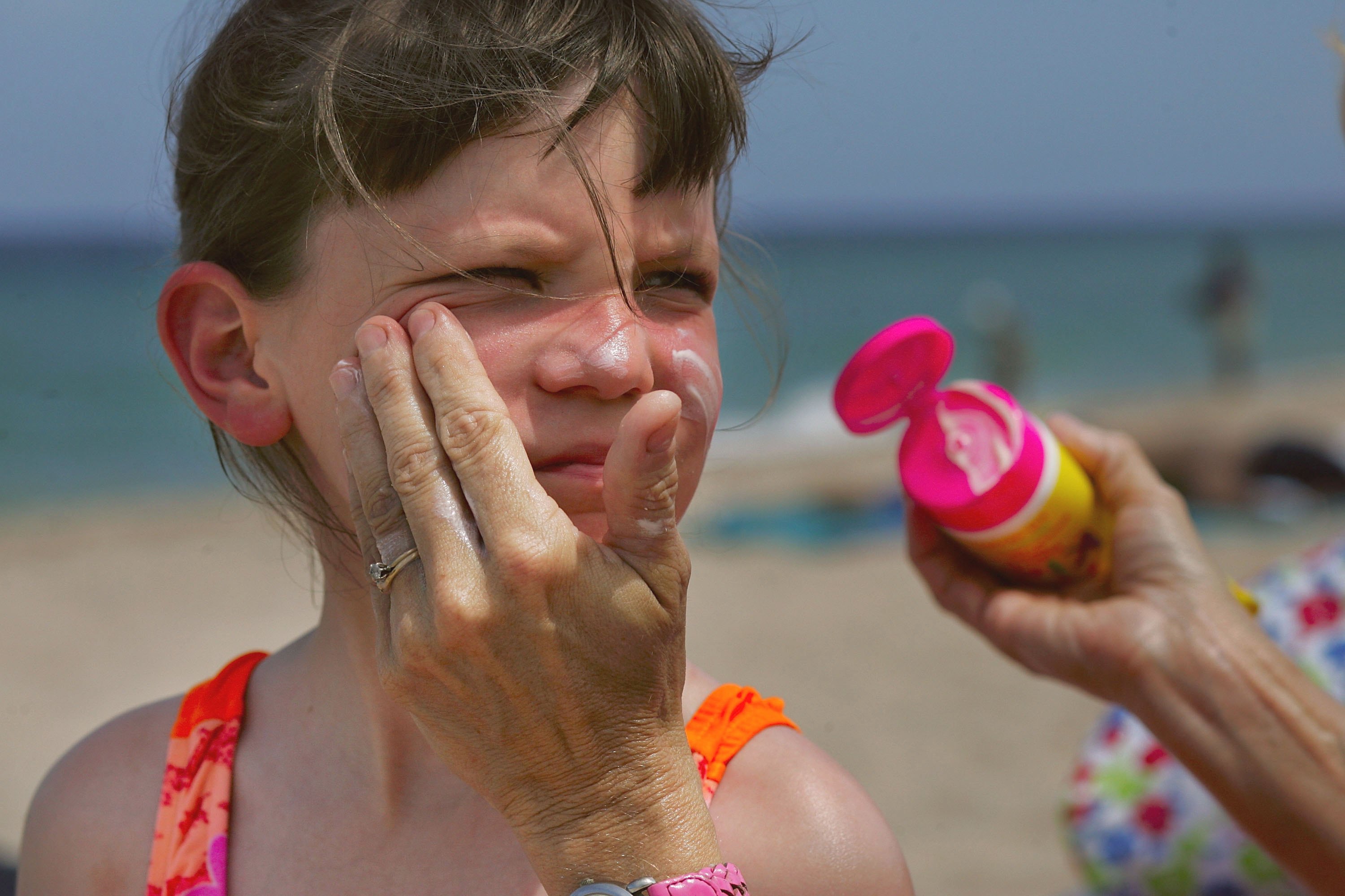 A woman puts sunscreen on a child&#039;s face.