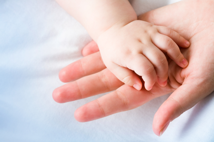 A baby and its parent touch hands.