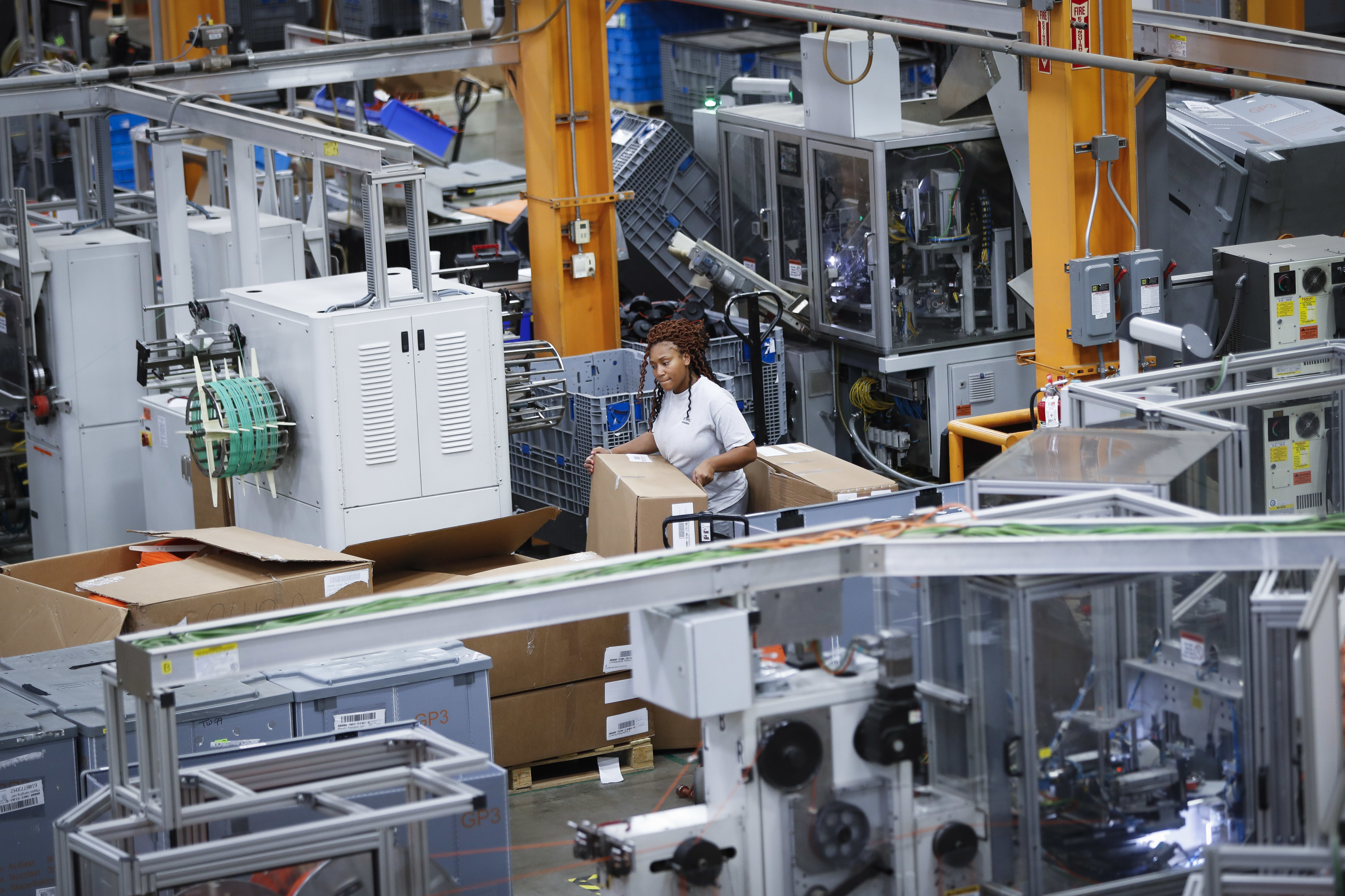 A woman works on the factory floor in a sea of robots.