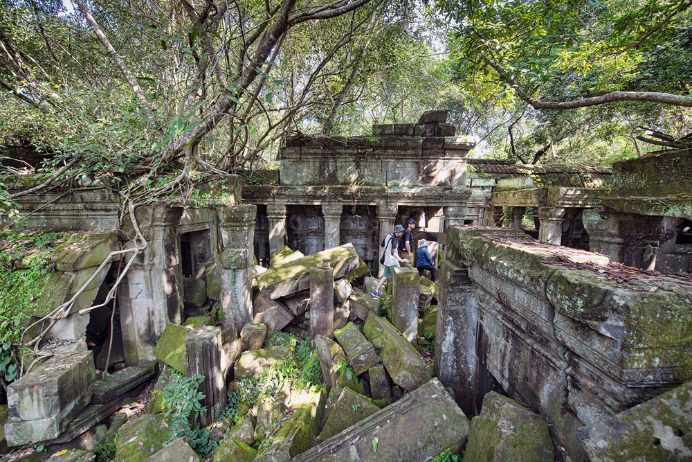 Visitors climb moss-covered stones in a section of a hidden temple.