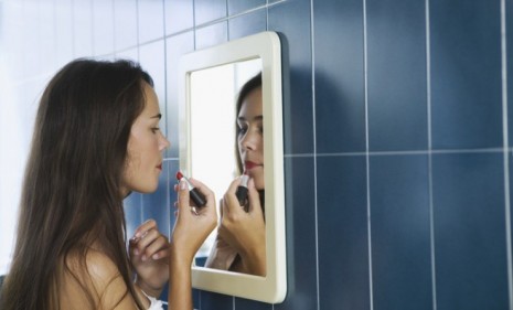 A teenage girl applies lipstick 