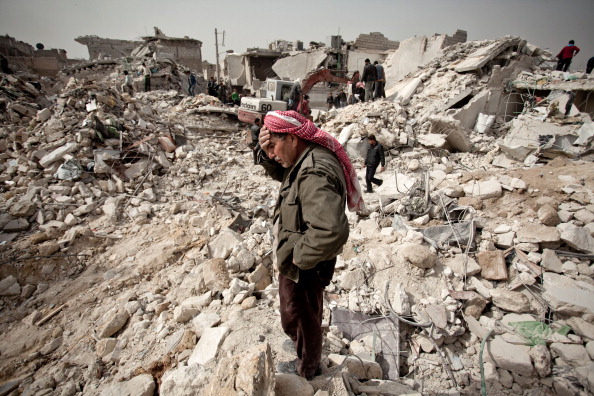 A Syrian man stands on the rubble of what used to be his house.