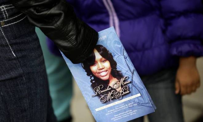 A mourner holds an obituary showing an image of Renisha McBride.