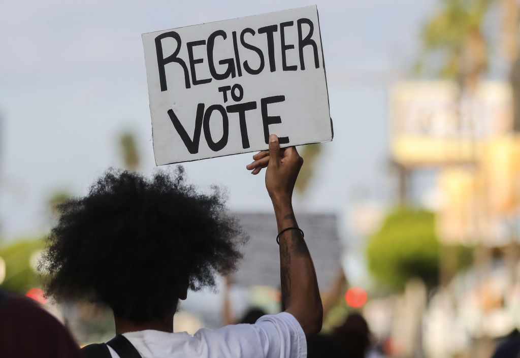 A protester carries a &#039;Register to Vote&#039; sign