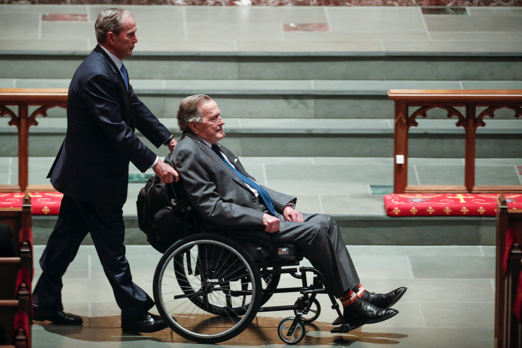 George W. Bush pushes George H.W. Bush in his wheelchair.