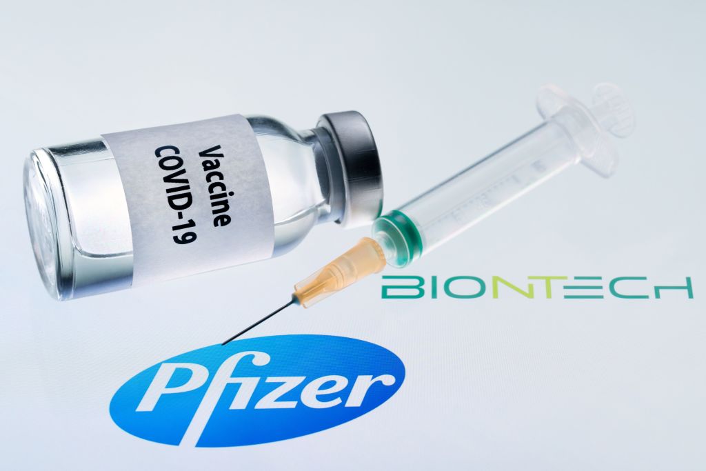 This illustration picture taken on November 23, 2020 shows a bottle reading &quot;Vaccine Covid-19&quot; and a syringe next to the Pfizer and Biontech logo