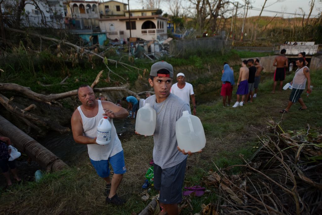 People in Puerto Rico carry water they found in a canal.
