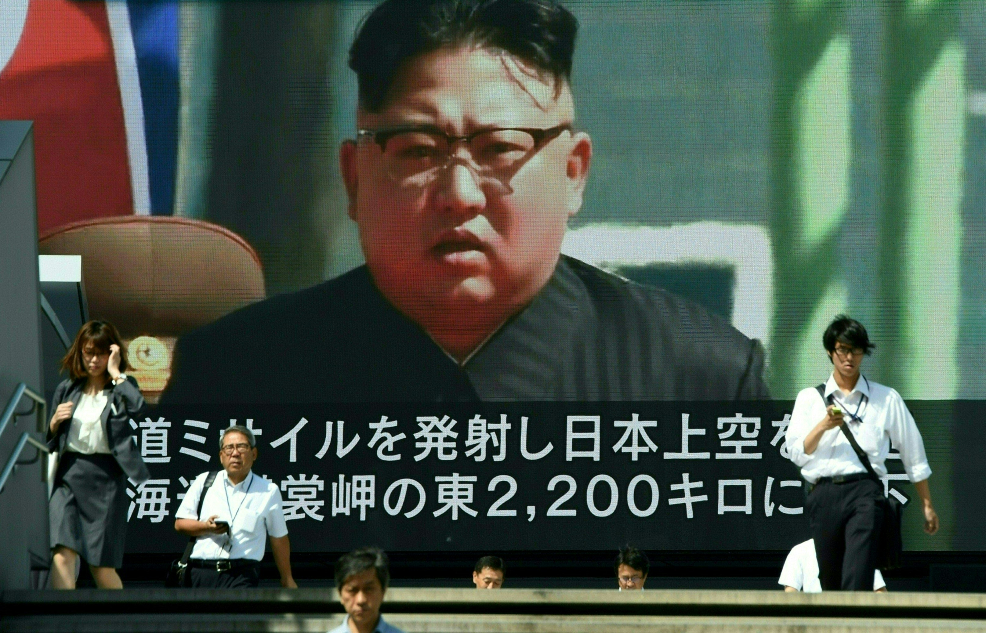 A video screen shows Kim Jong Un in Tokyo
