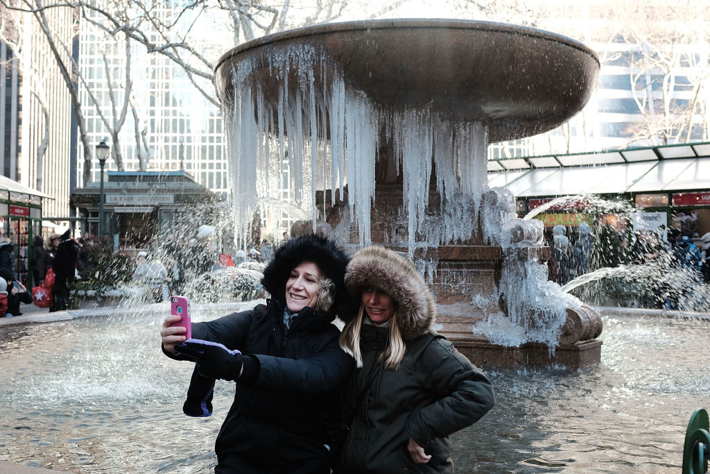 Two women take a selfie photo in front of a frozen fountain in Bryant Park on a frigid day in Manhattan on December 27, 2017 in New York City.