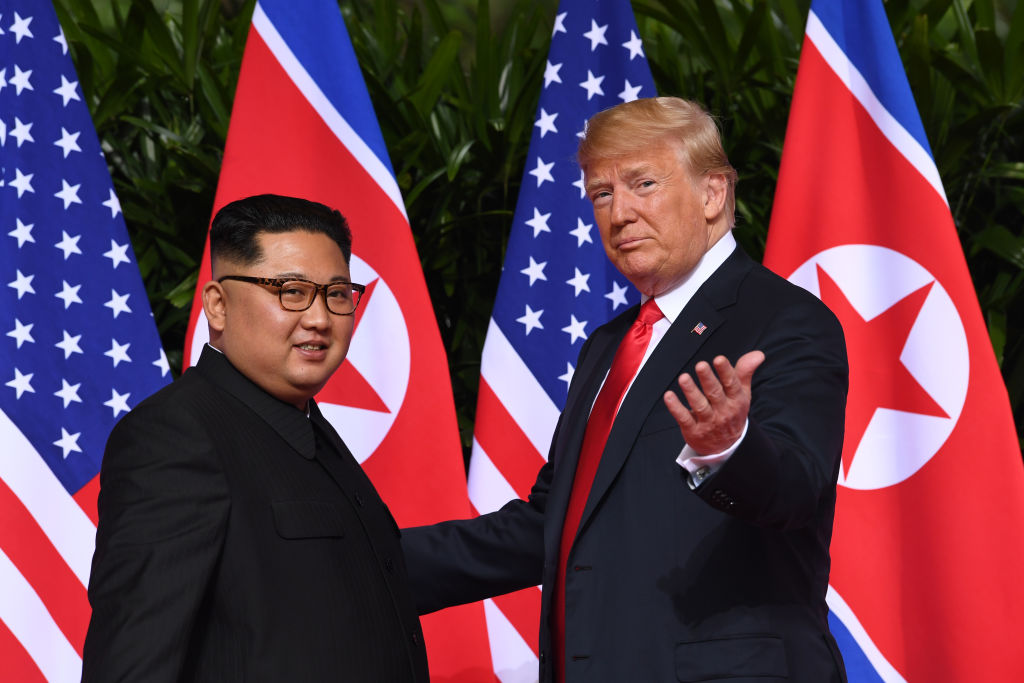 President Trump and Kim Jong Un meet in Singapore, with the American and North Korean flags in red white and blue behind them.