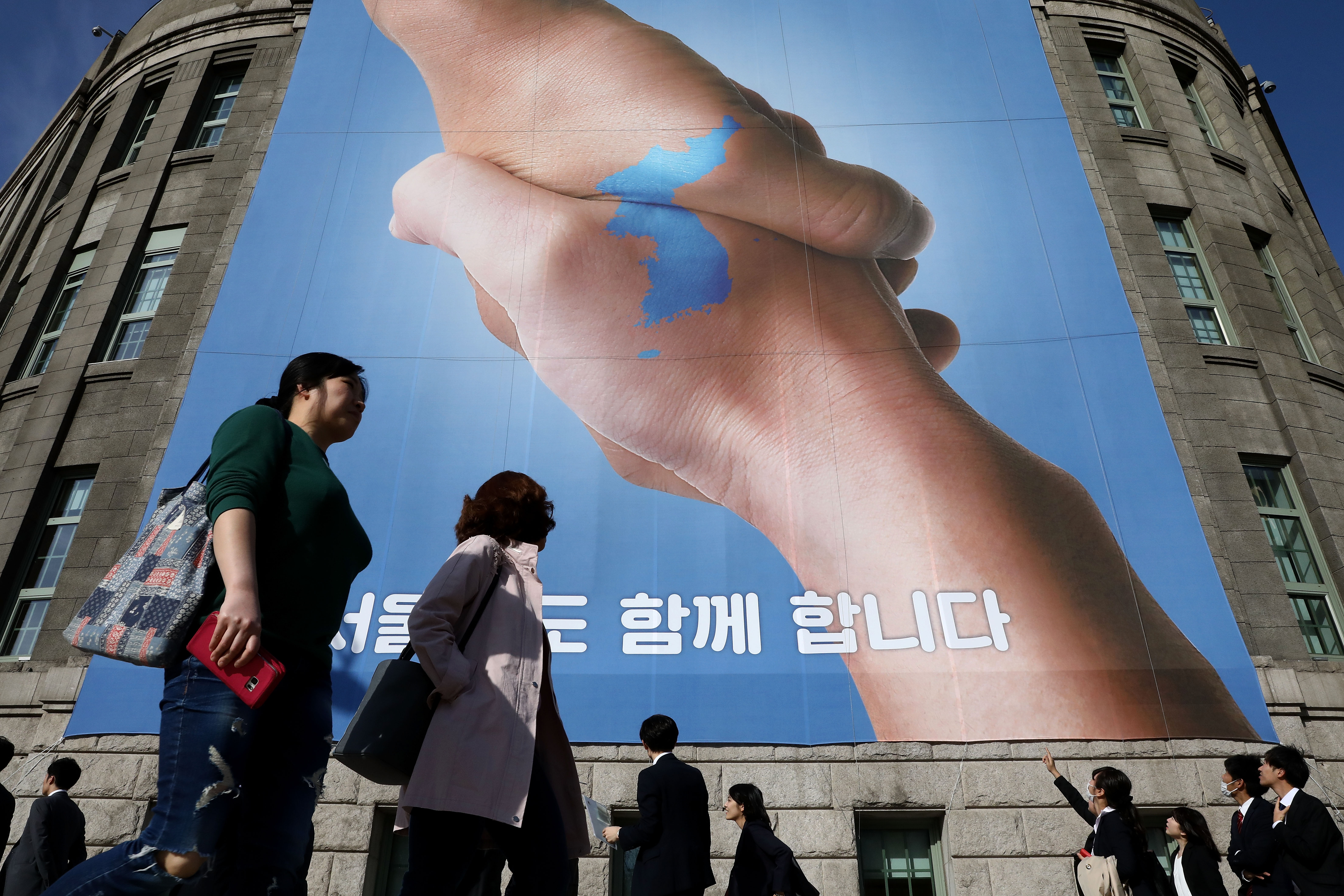  Pedestrians walk by a banner showing a map of the Korean peninsular to wish for a successful inter-Korean summit on April 21, 2018 in Seoul, South Korea.
