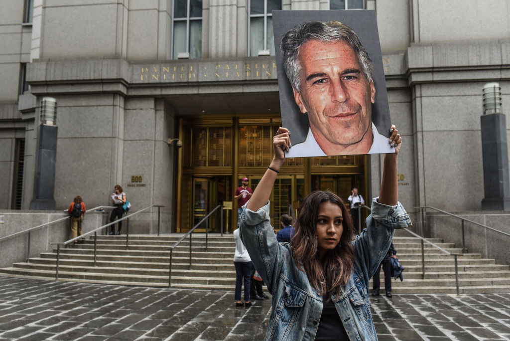 A woman holds a picture of Jeffrey Epstein.