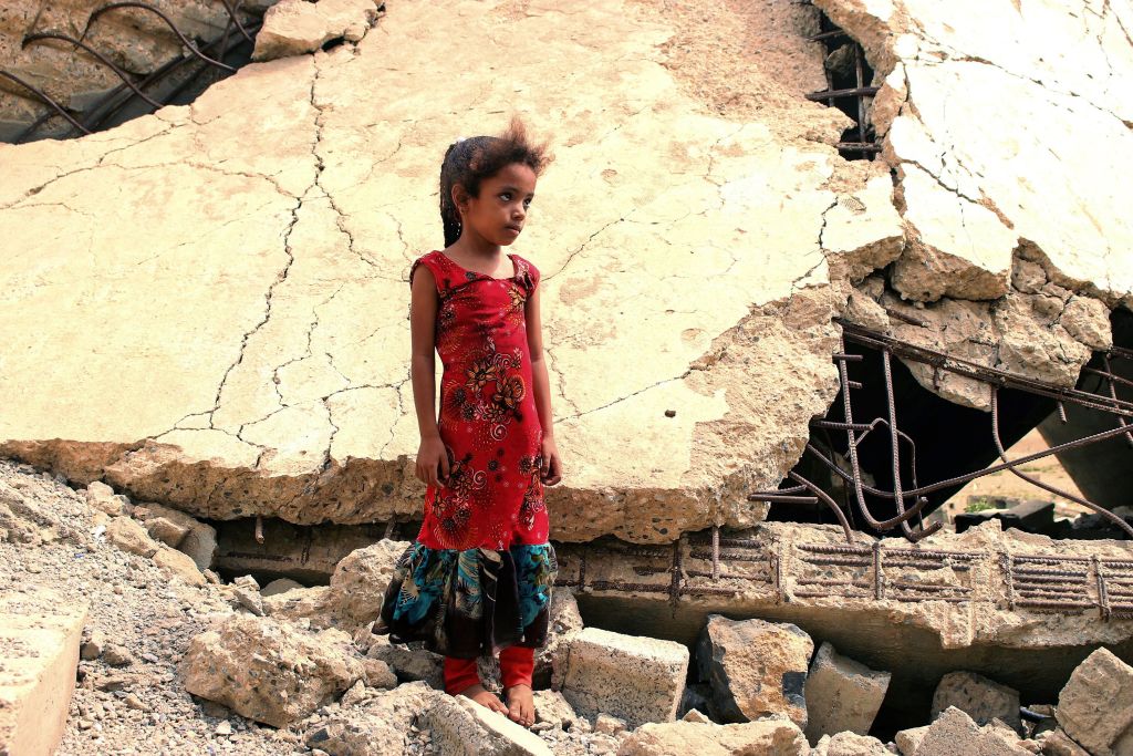 A displaced Yemeni girl stands in rubble.