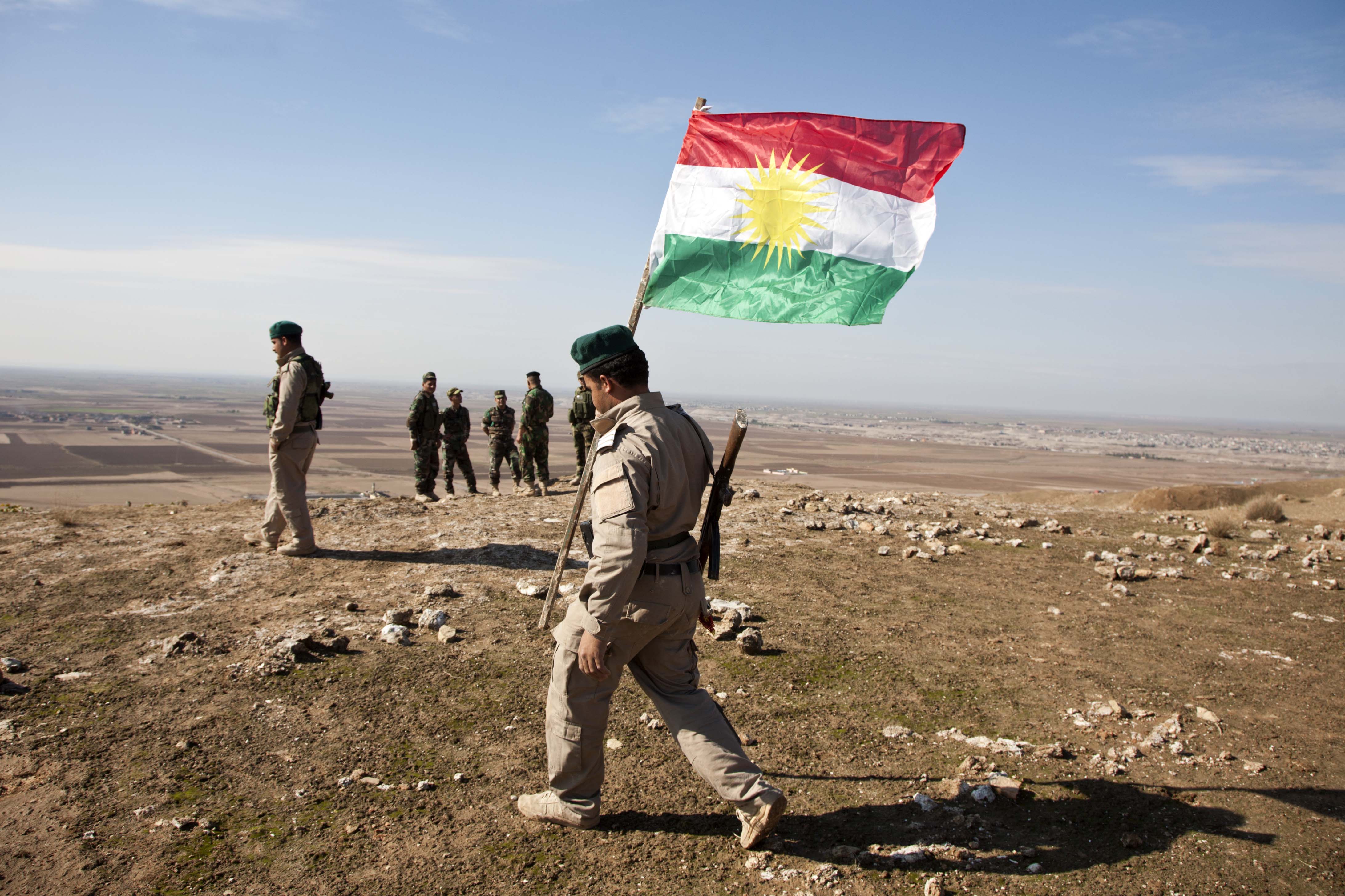 A Kurdish peshmerga fighter plants the Kurdish flag on top of a hill in the disputed territories.