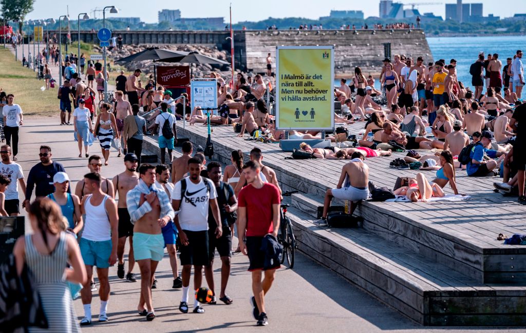 Young people enjoy the sun in Malmo, Sweden, around a sign encouraging social distancing