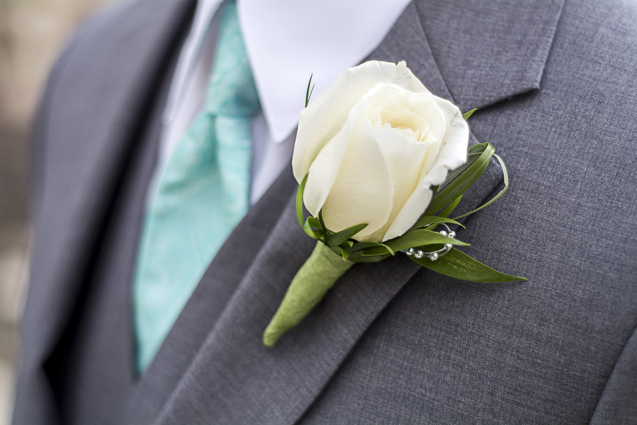 A person wearing a gray suit and a rose boutonniere.