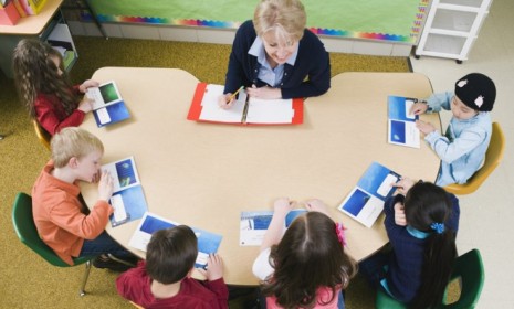 Kindergarten students sit at a table with their teacher: Using smiley, neutral, and sad faces to indicate grades, Georgia&#039;s five-year-olds will soon be tasked with evaluating their teachers&#039; 