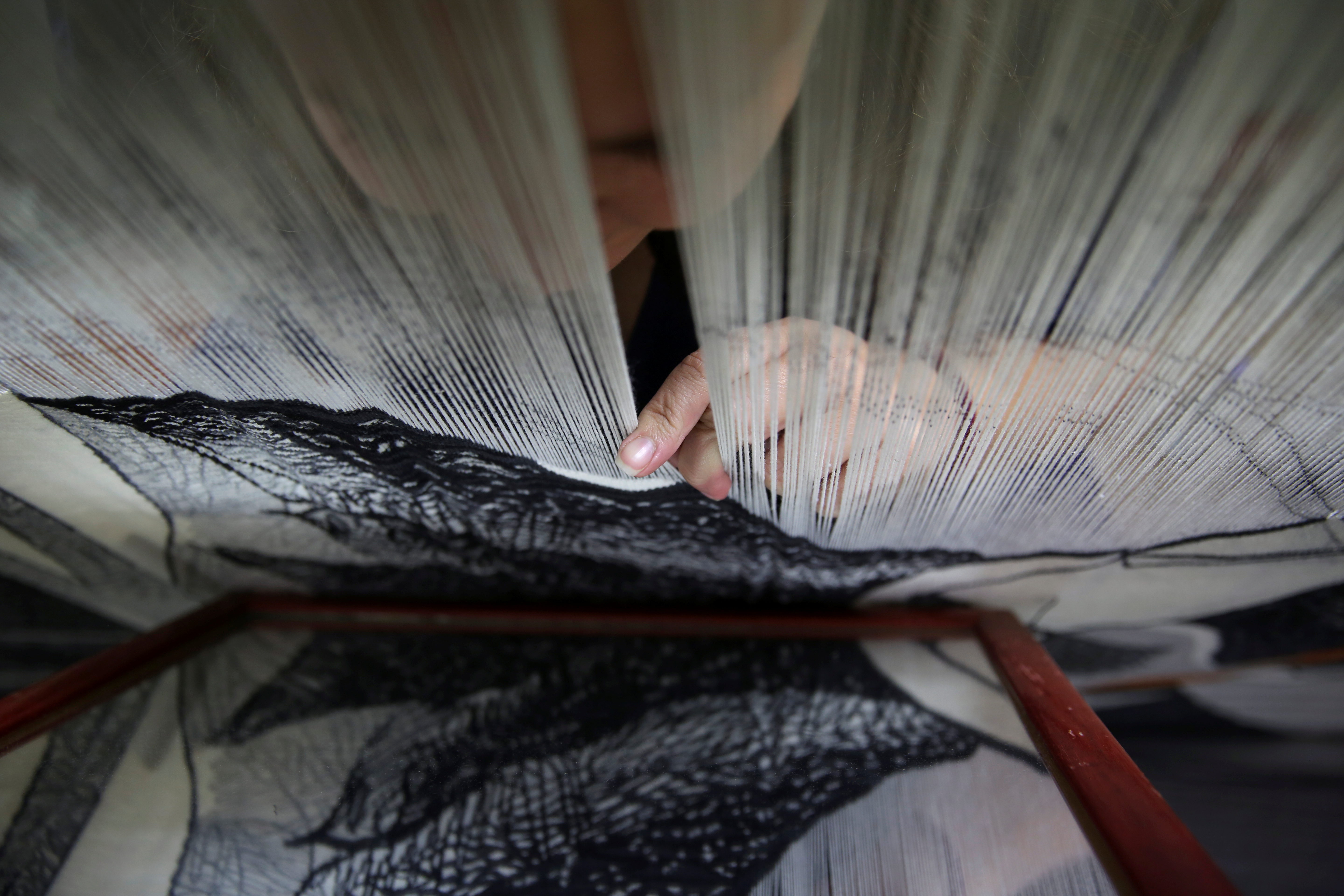 Marta Soria, 34, checks her work on a mirror as she hand-weaves a tapestry.