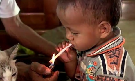 Another Indonesian toddler lights up a cigarette with the help of his grandfather: One third of the country&#039;s kids try smoking before the age of 10.