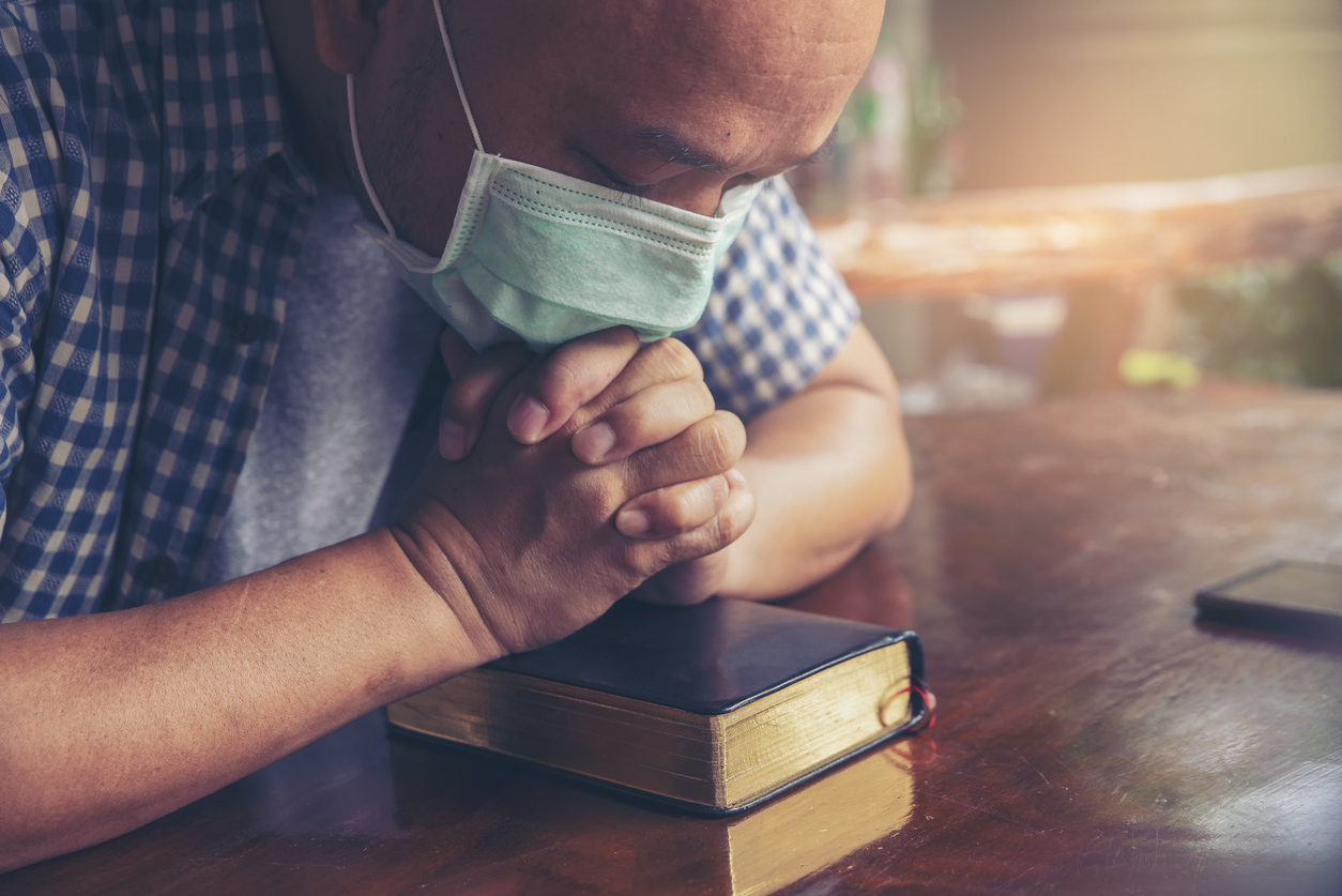 Man praying over Bible while wearing mask