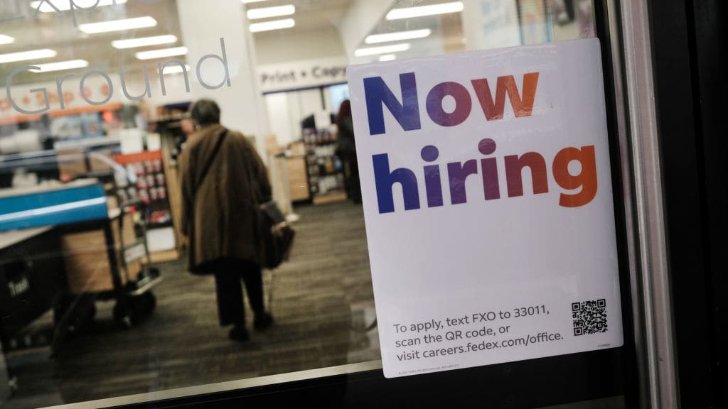 A &quot;now hiring&quot; sign on a store&#039;s door.