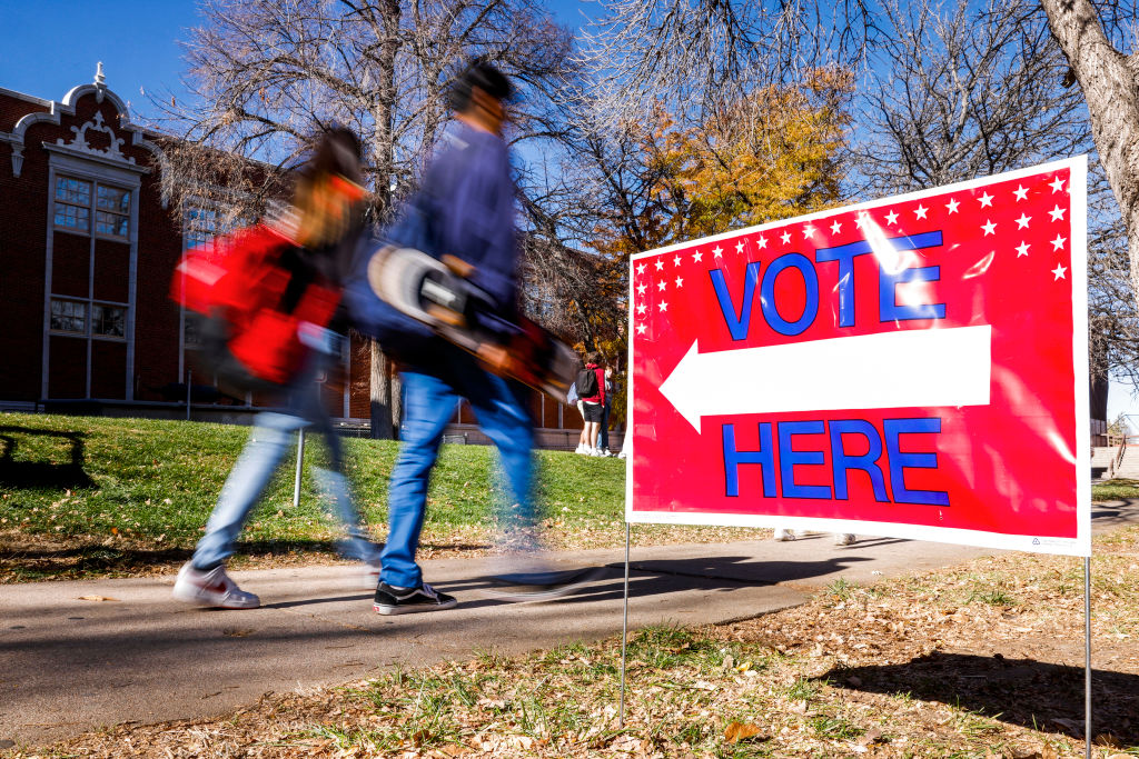 students walking past vote here sign, photo