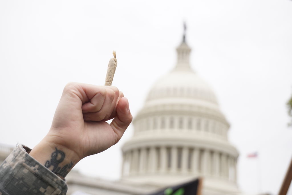 A clenched fist holding a marijuana joint in front of the U.S. Capitol