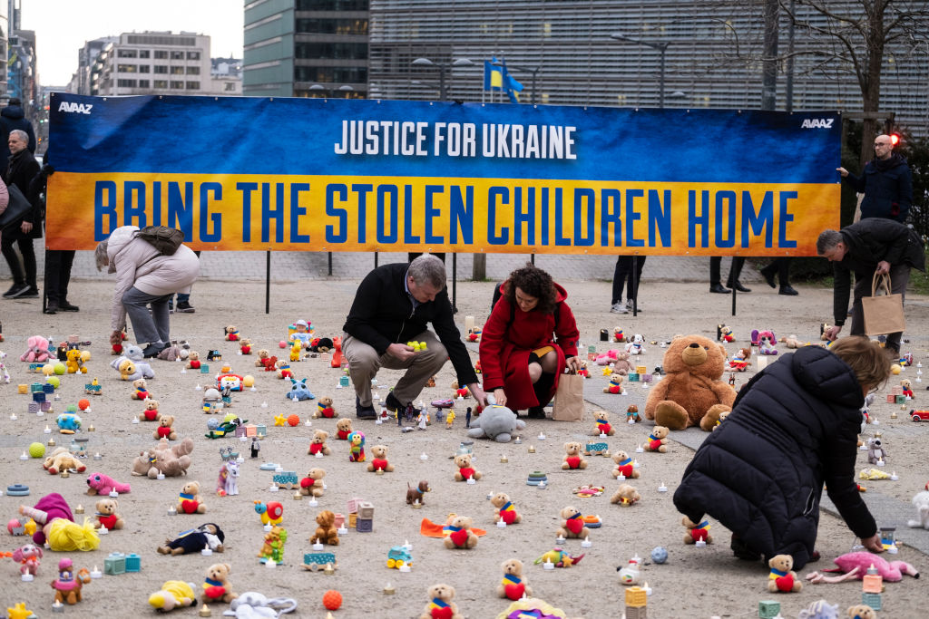 People from U.S.-based nonprofit organization avaaz light candles beside teddy bear in Schuman Roundabout.