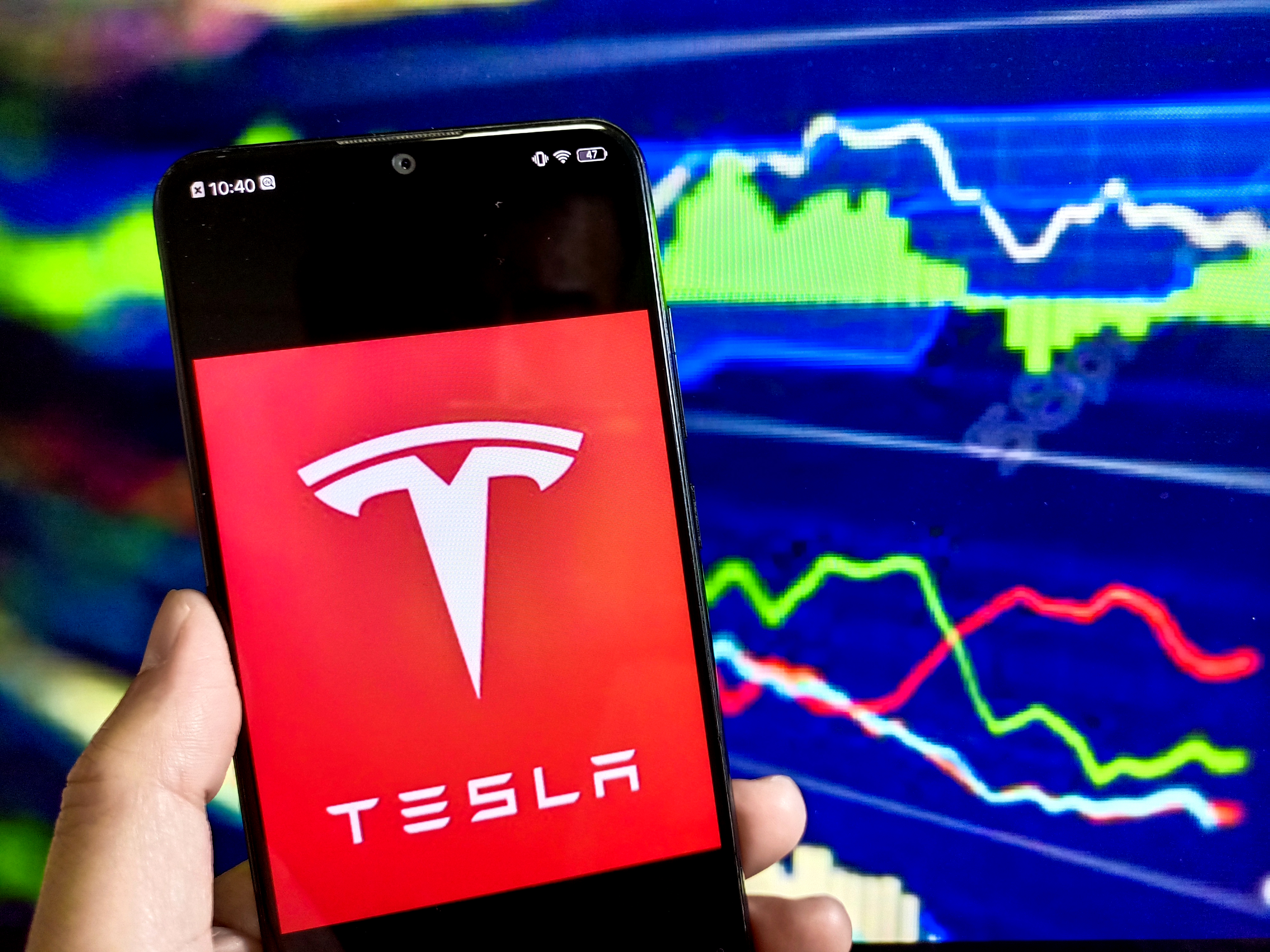 The Tesla logo on a phone in front of charts