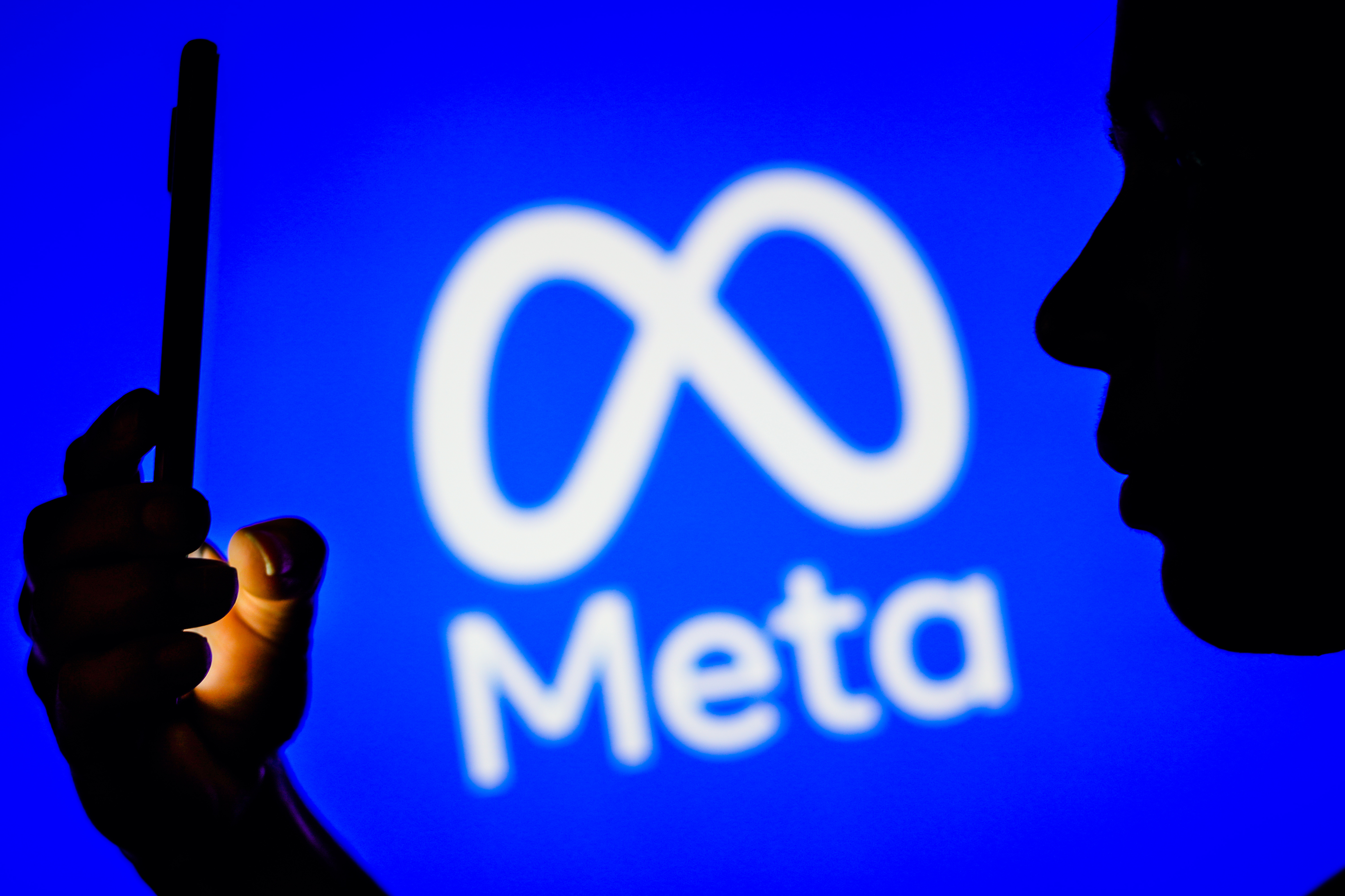 A photo of a person looking at a phone and a Meta logo in the background