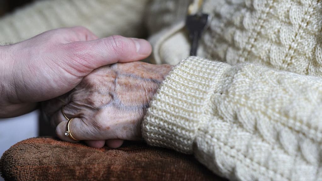 A woman holds the hand of an elderly Alzheimer&#039;s patient.