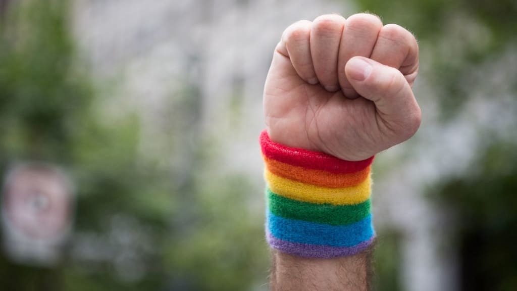 A man raises a fist while wearing a rainbow bracelet.