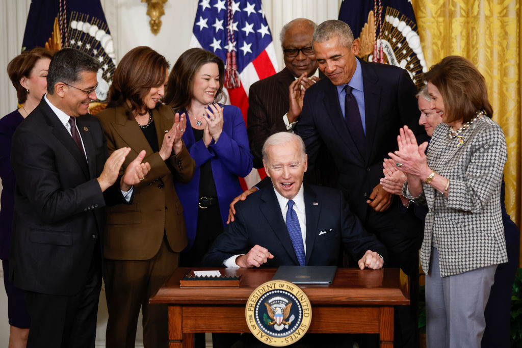 Joe Biden signing an executive order as Barack Obama, Kamala Harris, Nancy Pelosi, and others look on