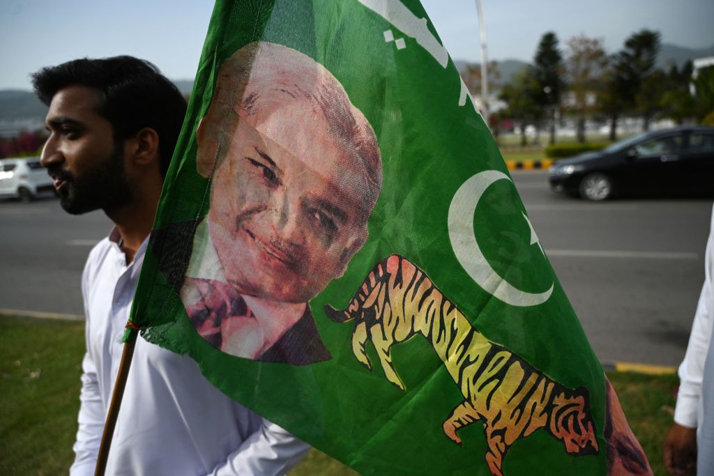 Pakistani man holding a flag with a picture of Shehbaz Sharif