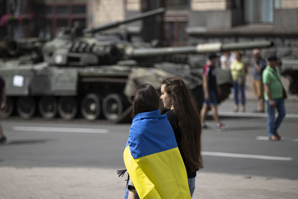 Woman wearing Ukrainian flag walks by a tank.