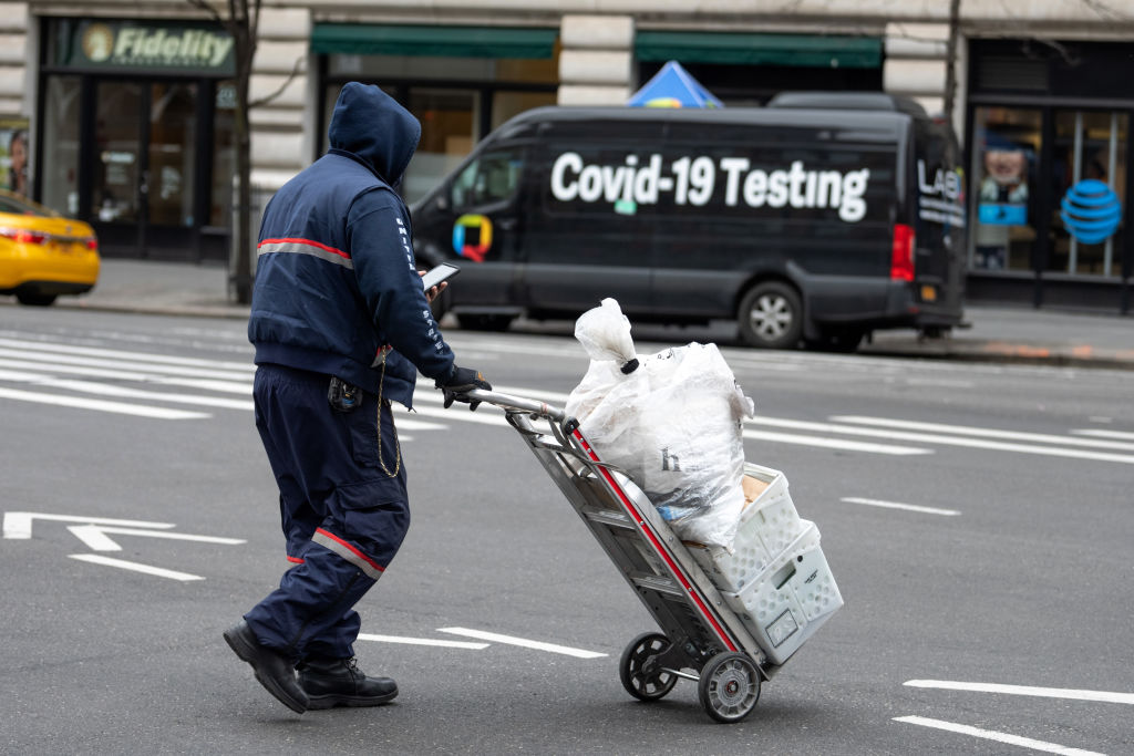 A USPS mail worker wheels a mail cart past a &quot;COVID-19 Testing&quot; location 